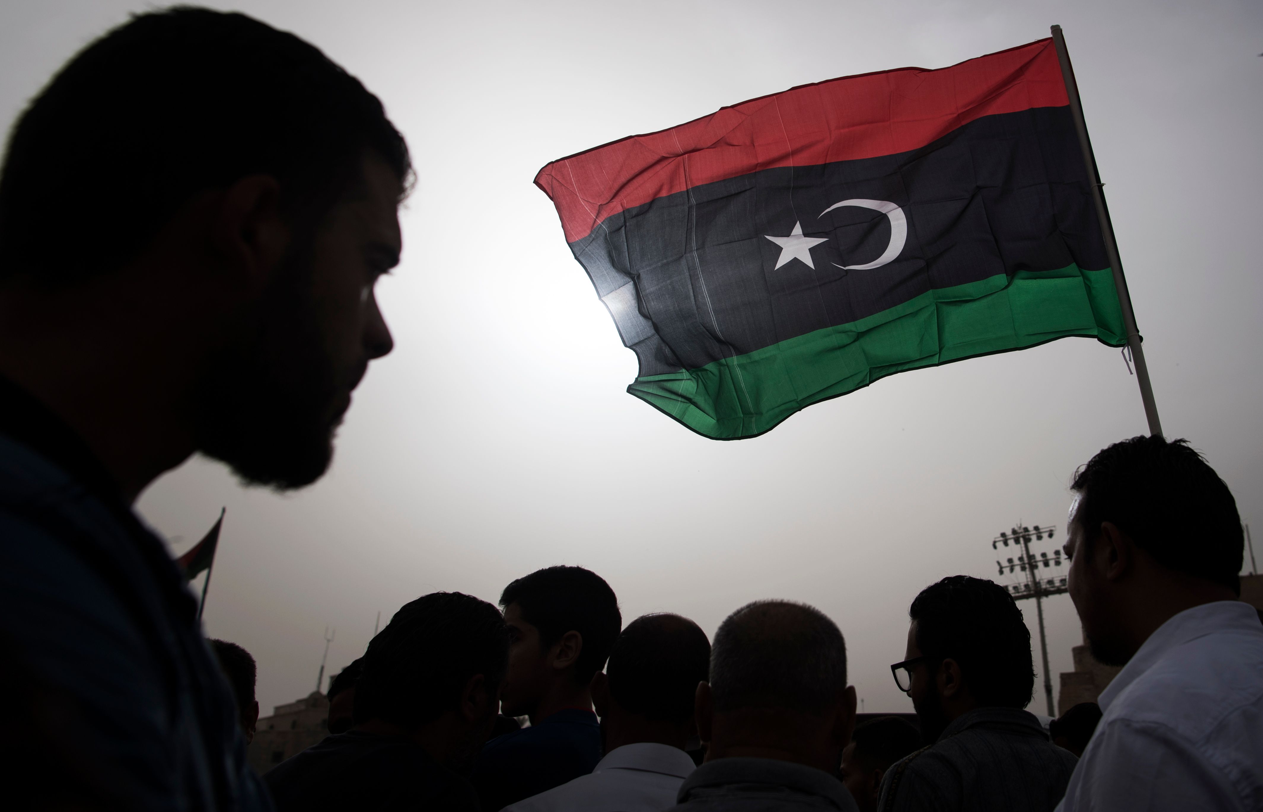 Libyan flag flying high with silhouetted crowd in background