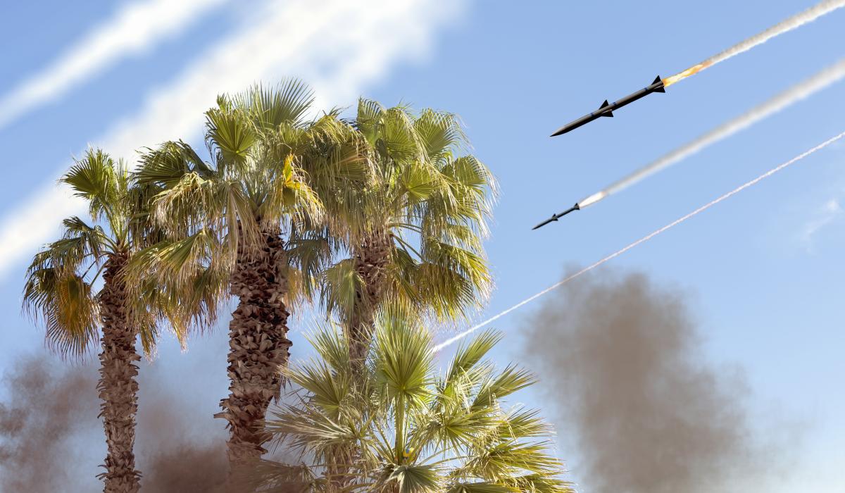 Missiles flying over palm trees with smoke and blue sky
