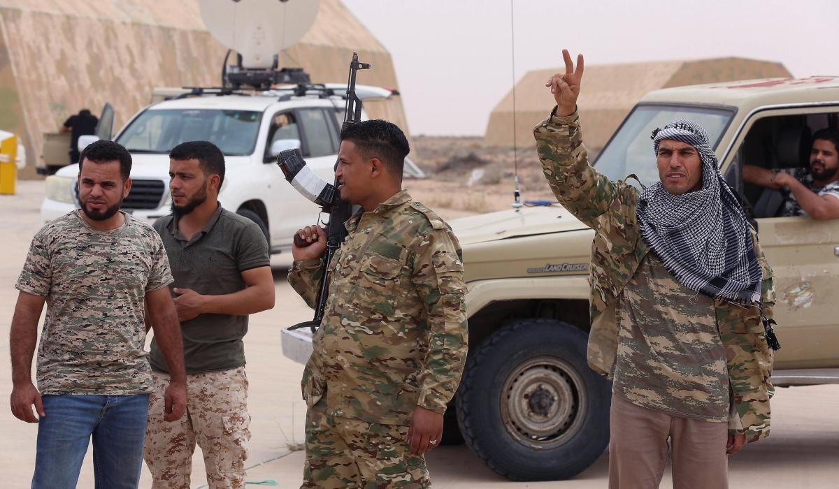 Military personnel with vehicles in desert, one making victory sign