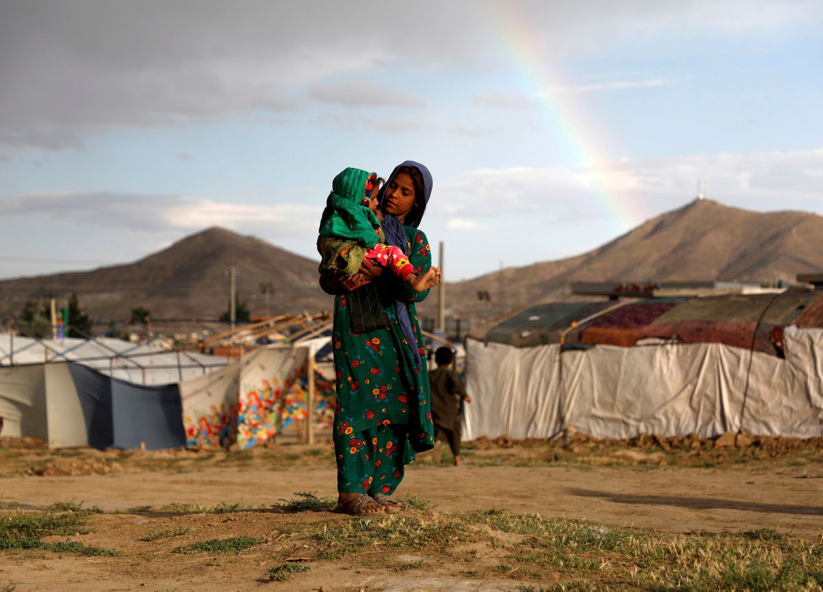 Woman holding child in refugee camp with rainbow and mountains backdrop