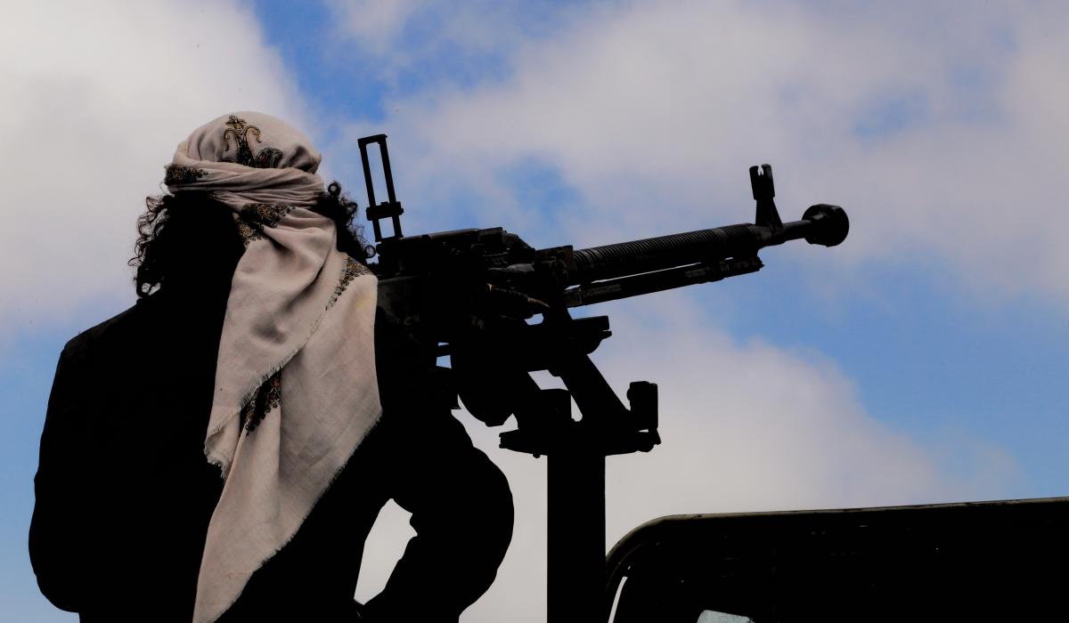 Silhouette of a person with a covered head operating a mounted machine gun