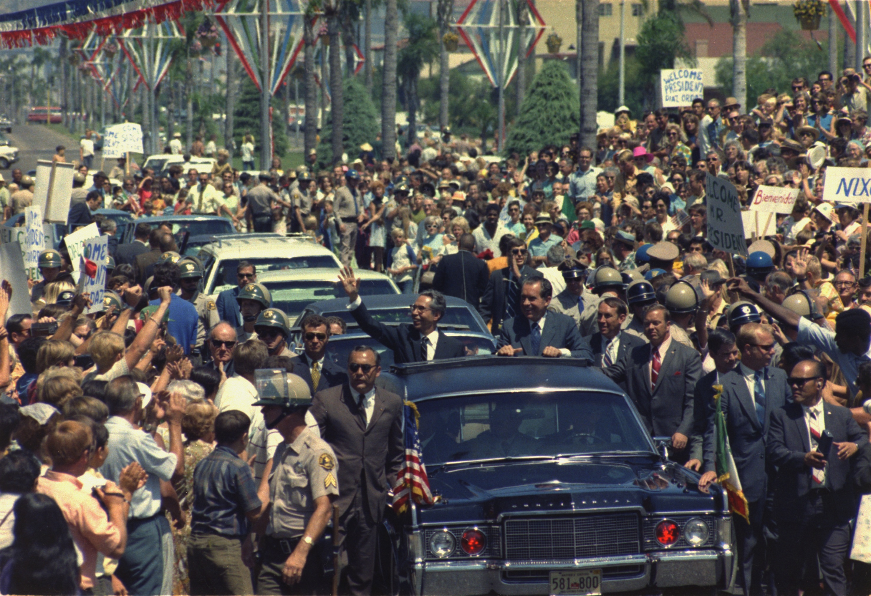 President surrounded by crowds and security during public motorcade in 1960s