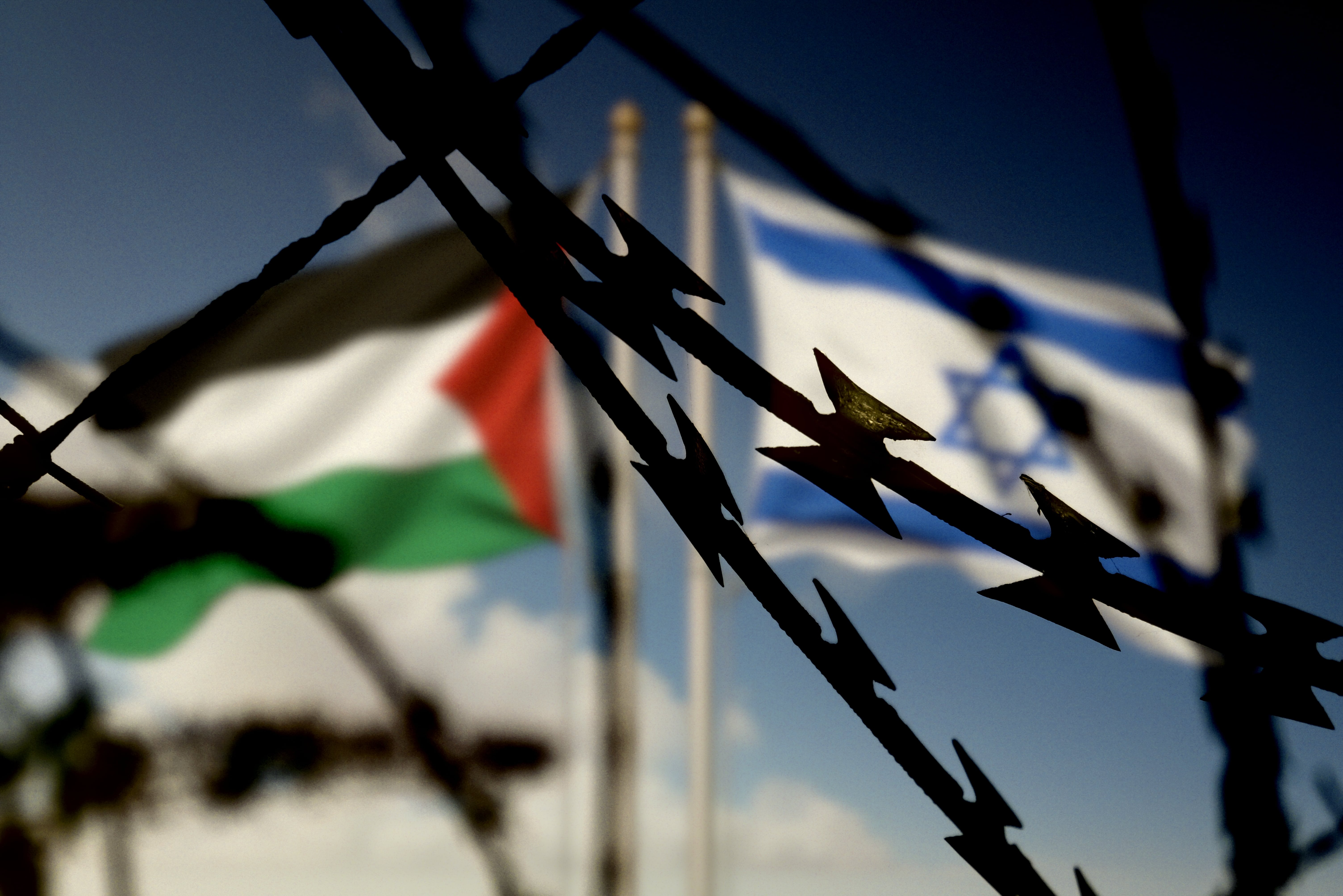 Barbed wire separating Palestinian and Israeli flags, symbolizing conflict
