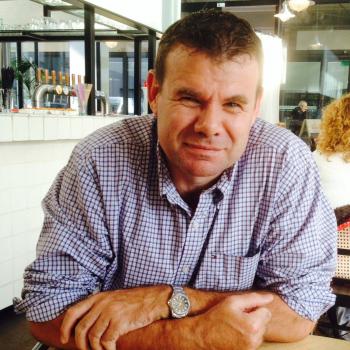 Middle-aged man in checkered shirt sitting at cafe table looking serious