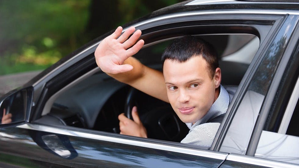 Conducteur faisant un signe de courtoisie au volant