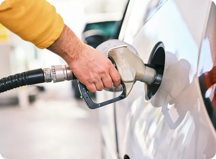 Hand holding a fuel nozzle while refueling a silver car.