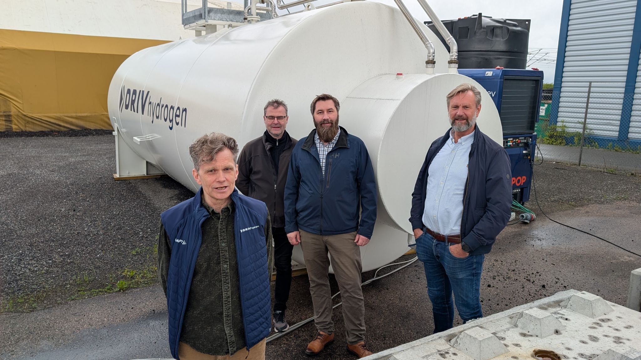 Aage Bjørn Andersen, Jon Eriksen, Terje Paulsen og Frank Sagvik foran en stor tank med Driv Hydrogen-logo på siden