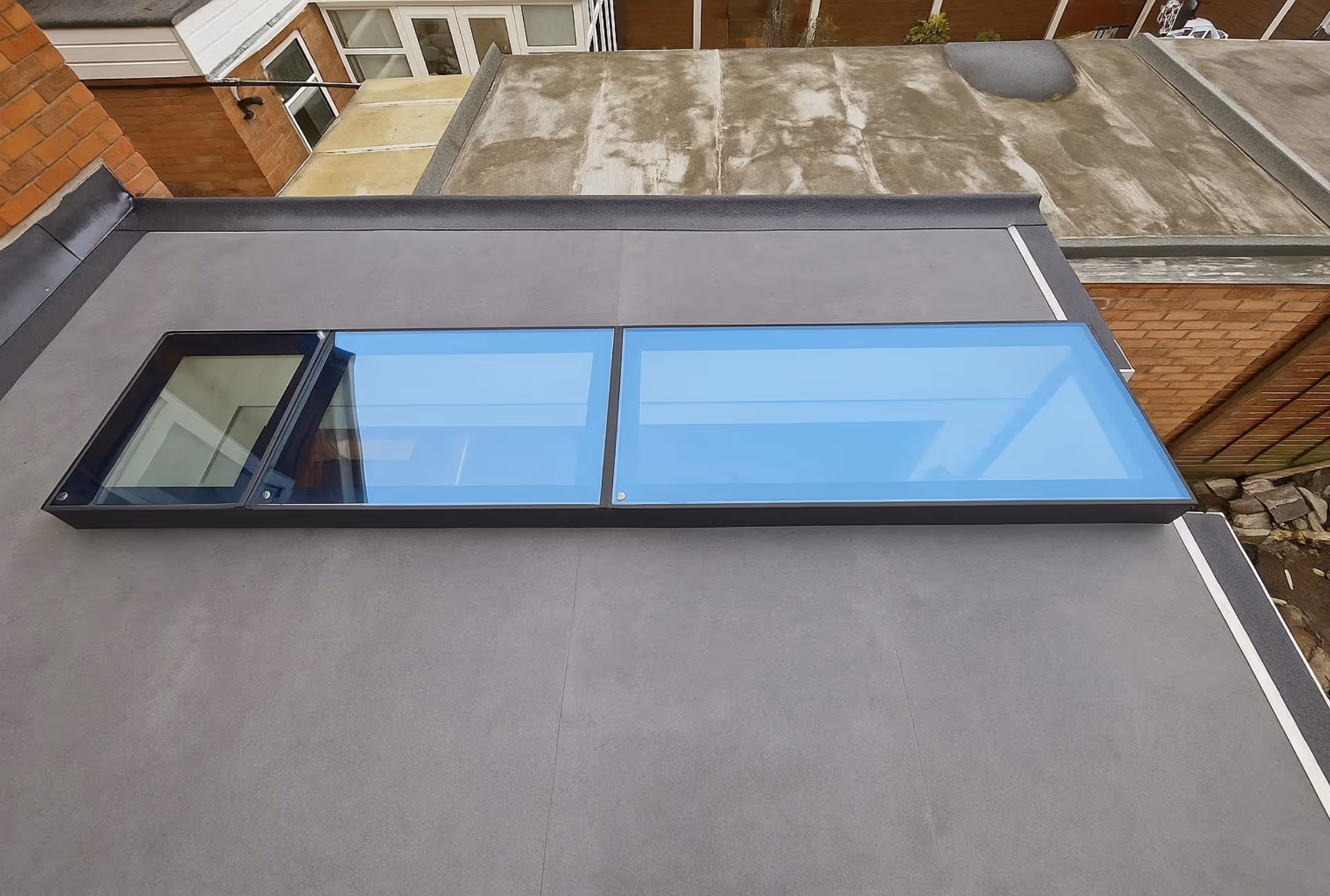 Flat roof with black-framed skylight featuring three double-glazed glass panels, allowing natural light into the building below.