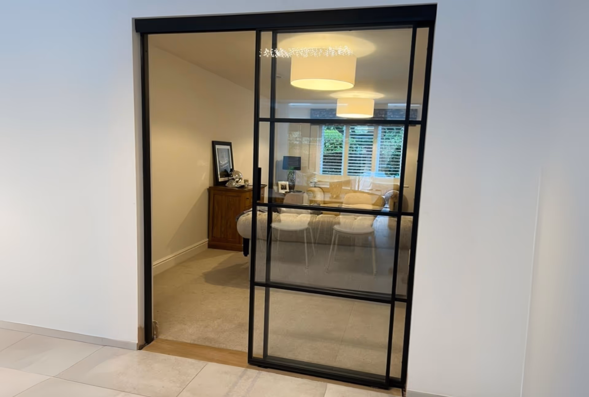 Black heritage-style glass door opening into a living room with beige carpet, wooden sideboard.