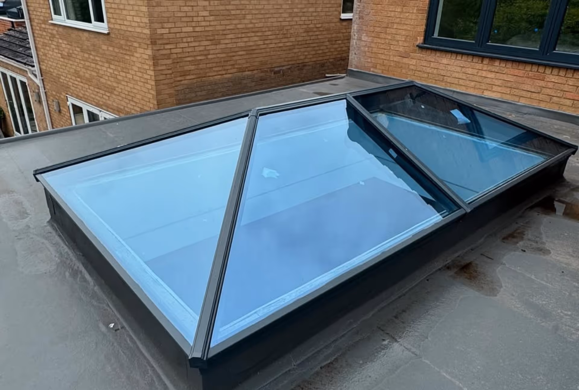 A single pyramid-shaped skylight on a flat roof, reflecting the blue sky and adjacent buildings.