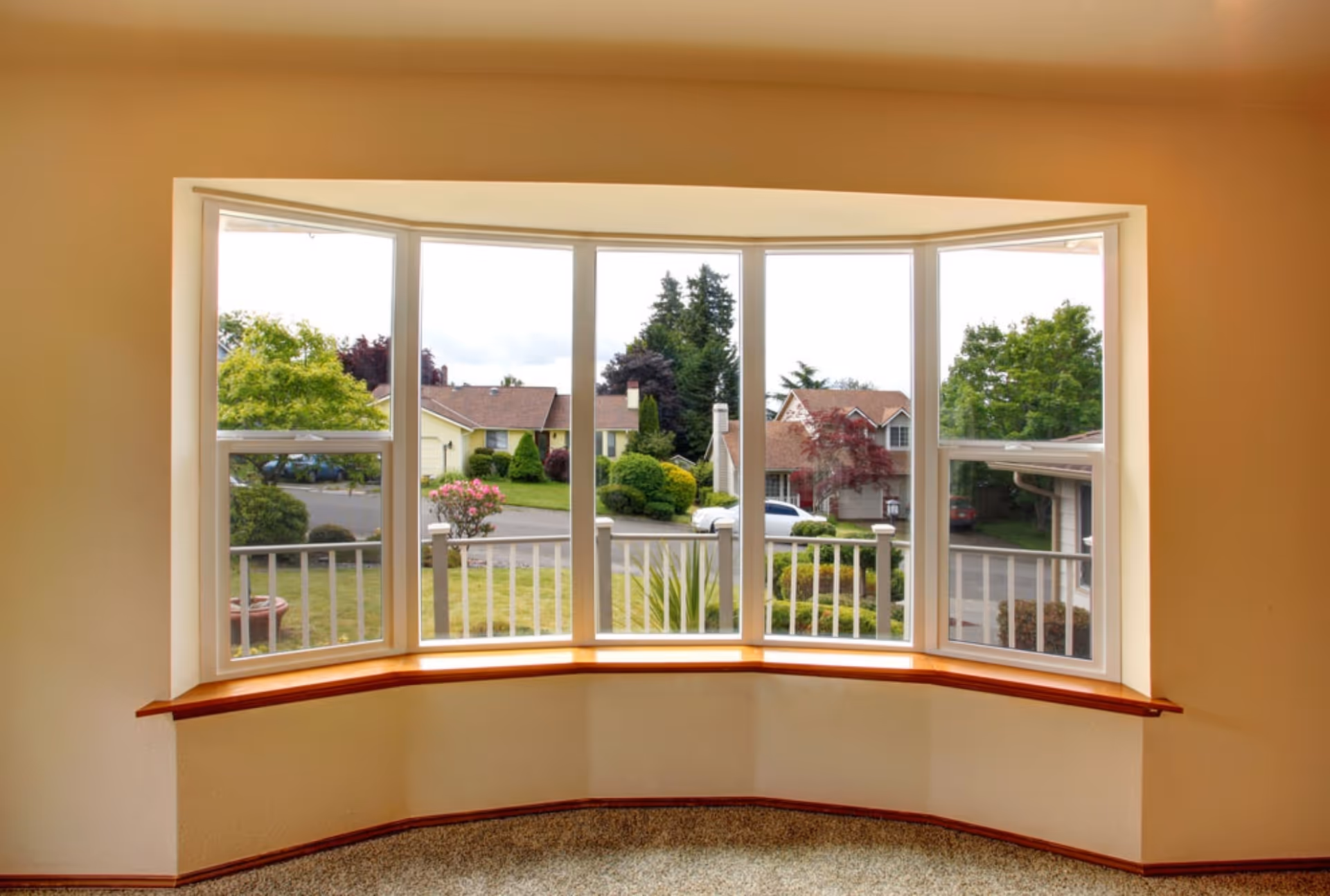 Spacious interior view of a wide bow window, offering panoramic views of a suburban street with houses and green gardens.