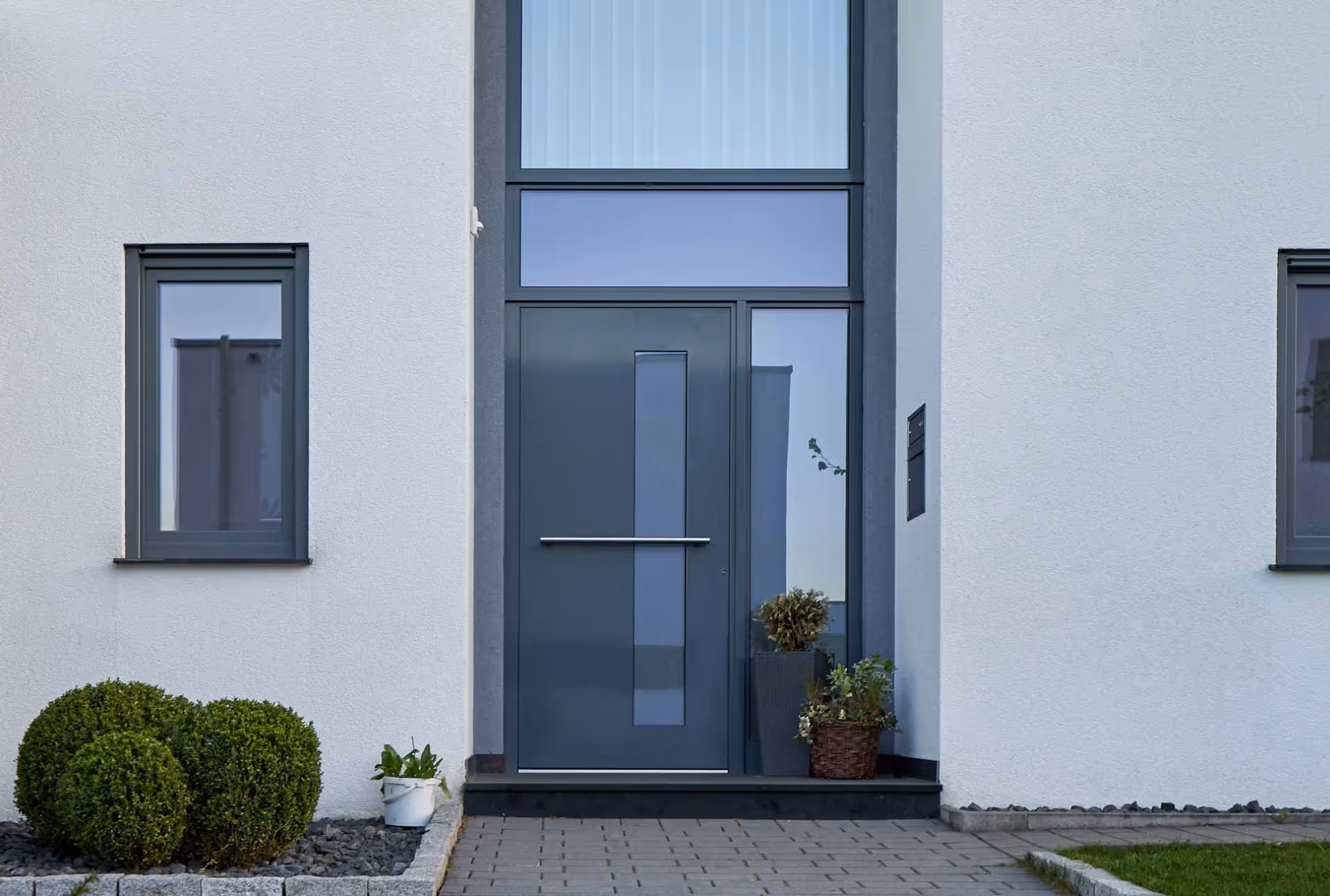 Grey aluminum door with central glass panel, side windows, and white exterior.