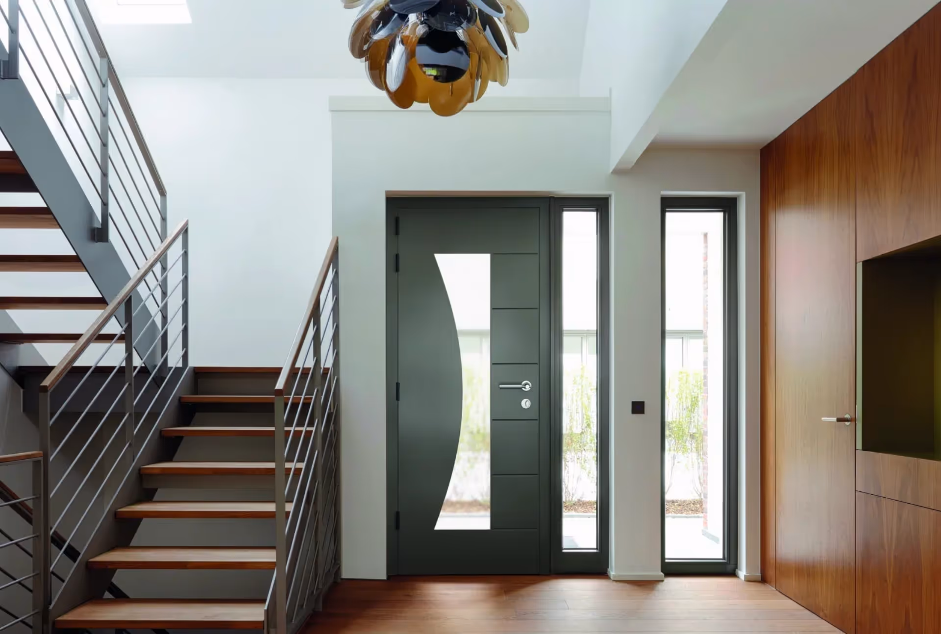 Dark aluminum door with curved glass design, flanked by tall windows in a modern interior.