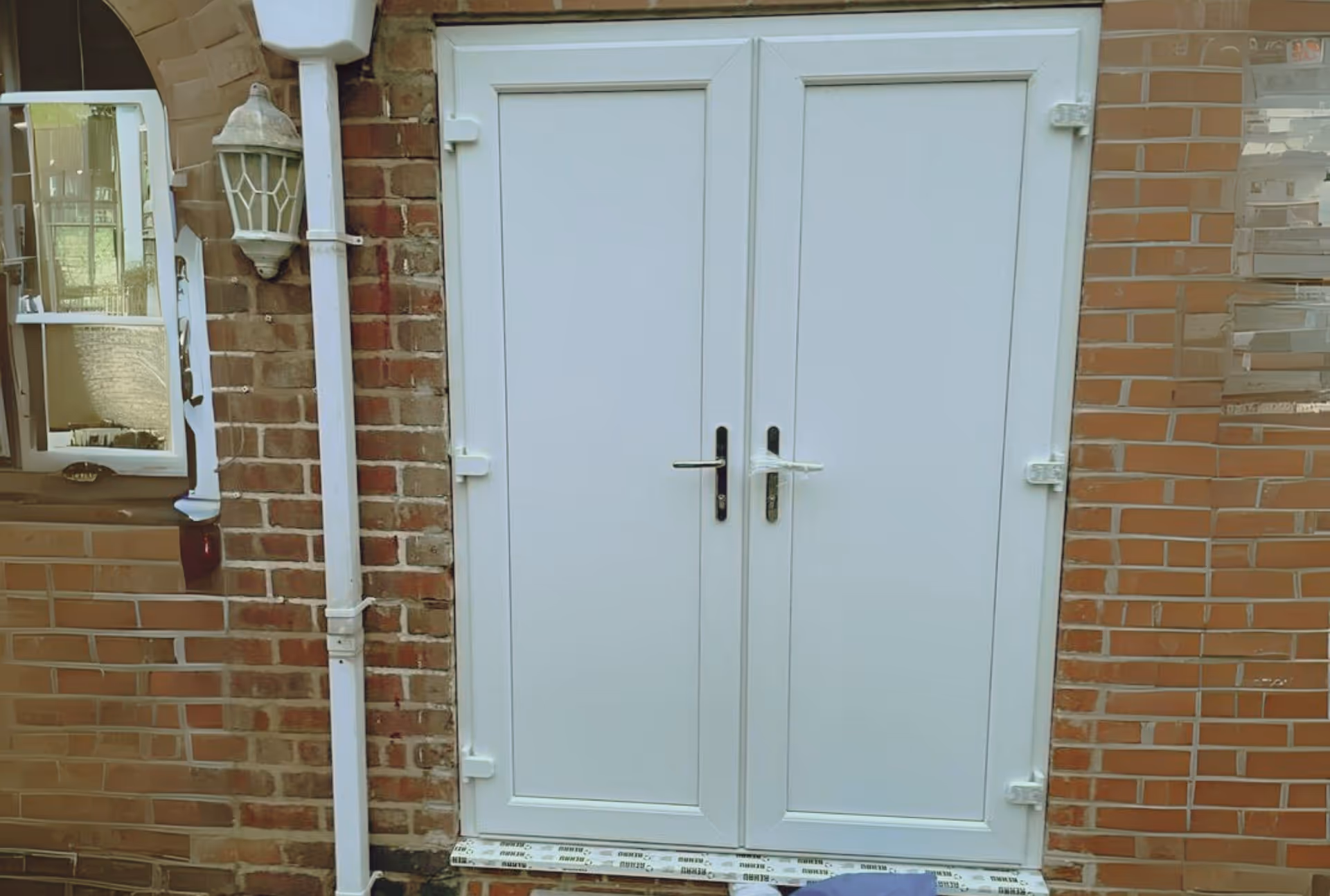 White uPVC double doors with black handles set in a brick wall.