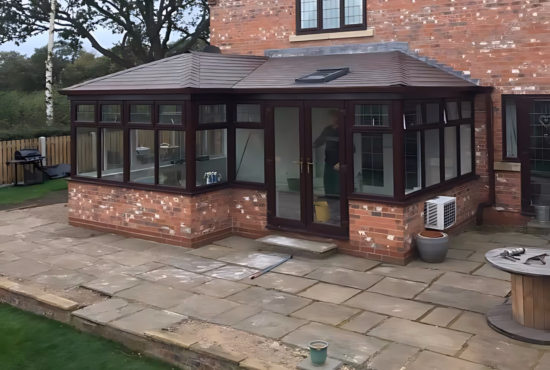 Brick house with a conservatory featuring dark window frames and a solid roof, designed for enhanced privacy and insulation.