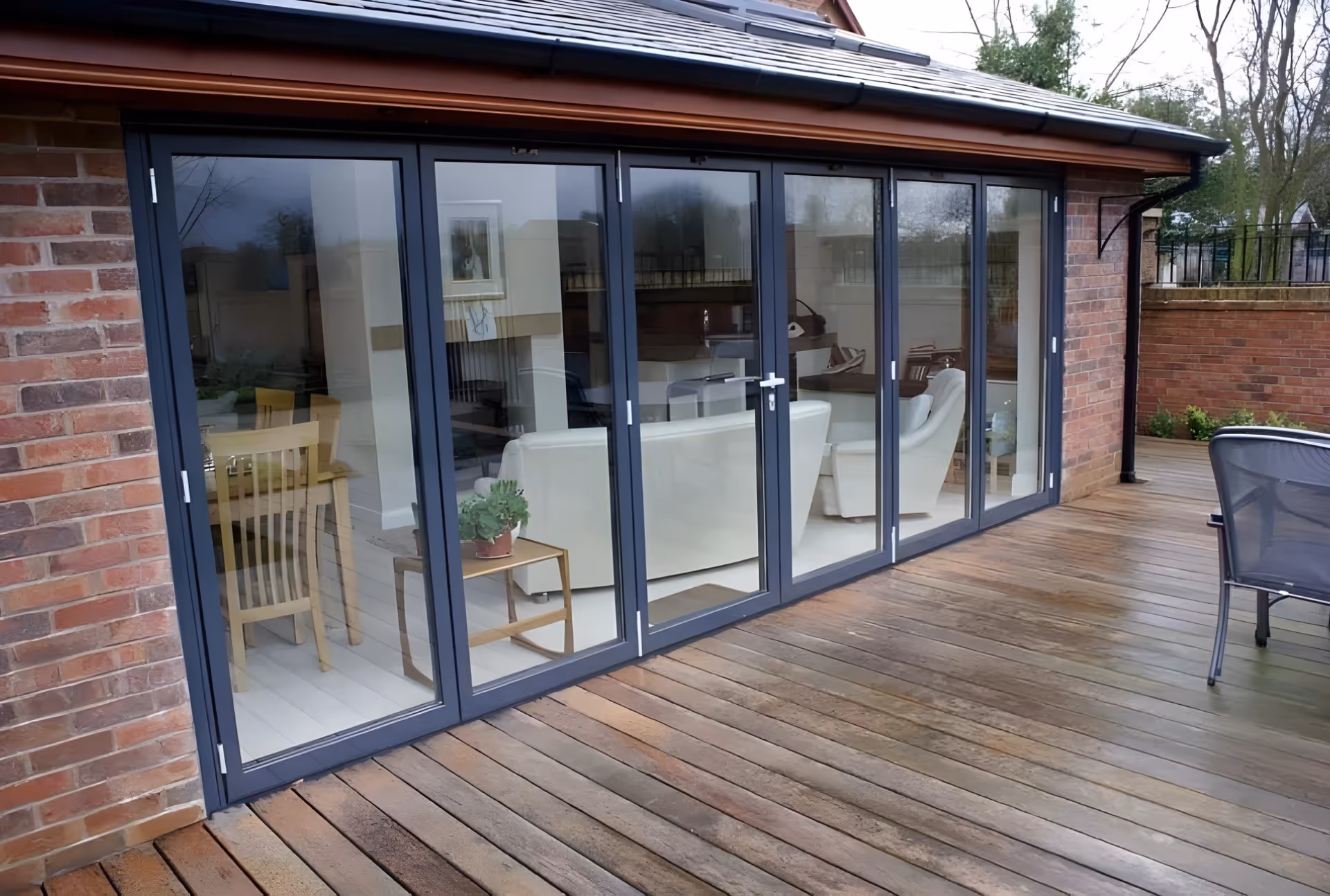 Dark-framed sliding glass doors opening from a house onto a wooden deck, with indoor furniture and potted plants visible through the glass.