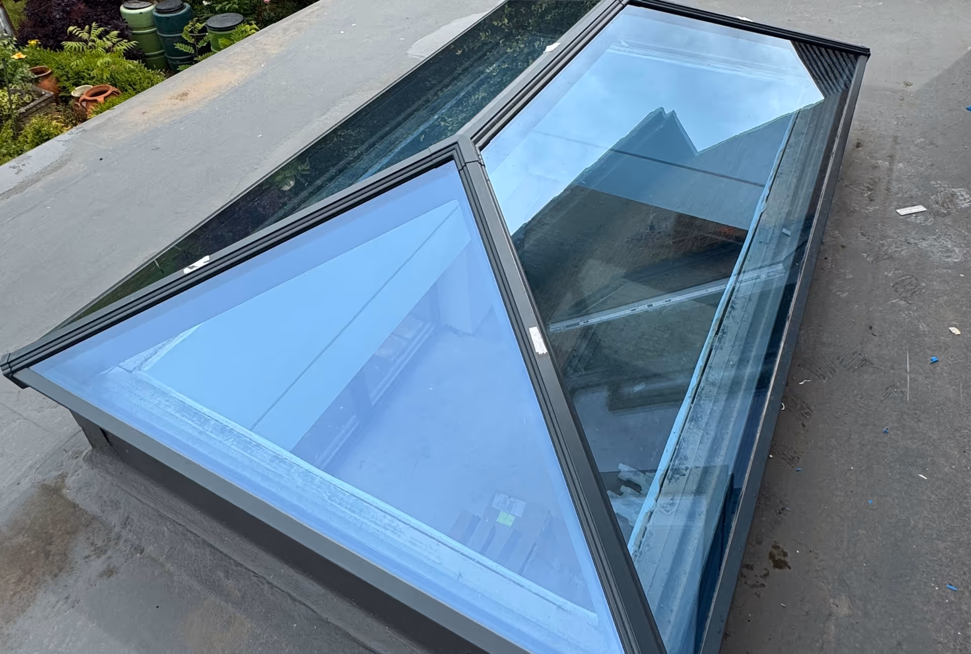 A close-up view of a pyramid-shaped skylight on a flat rooftop, showing reflections of nearby buildings and trees.