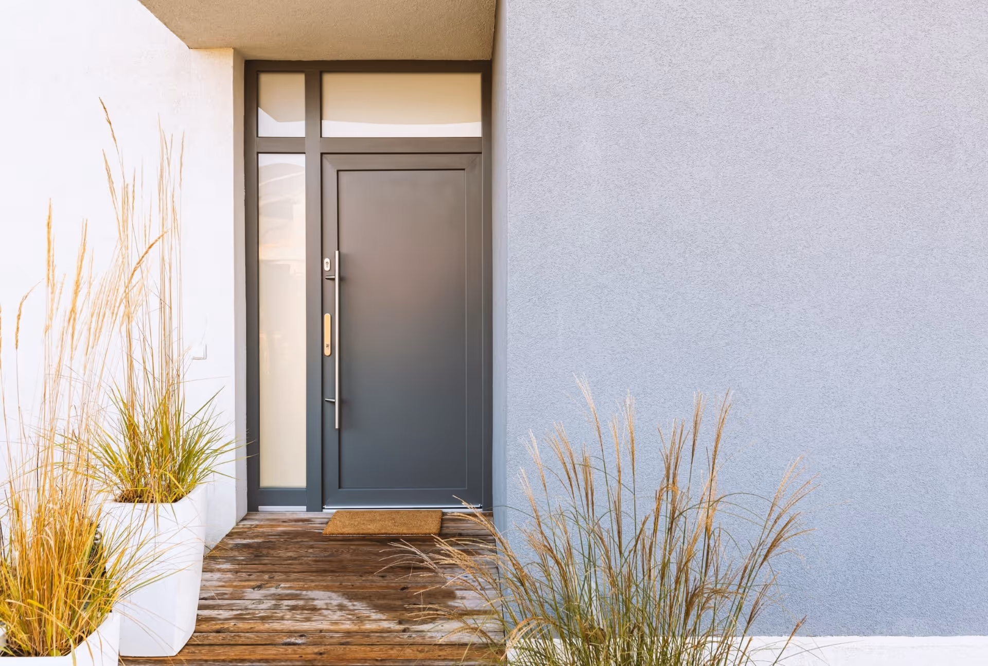 Dark grey aluminum door with glass panels, white planters, and light-toned exterior.