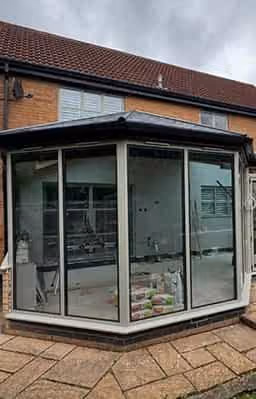 Newly built conservatory with large glass panels and dark roof, showcasing ongoing interior work with visible construction materials.