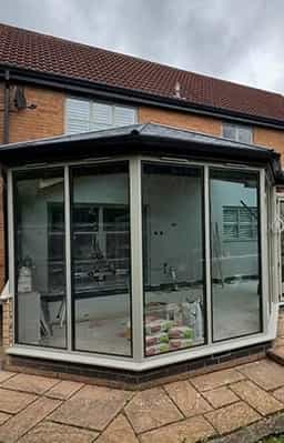 Newly built conservatory with large glass panels and dark roof, showcasing ongoing interior work with visible construction materials.
