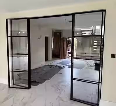 Modern glass conservatory with white-framed windows and doors on a brick home, highlighting window and door manufacturers.