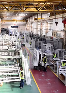 Workers collaborate in a bright industrial factory with large windows, showcasing a dynamic and productive environment.