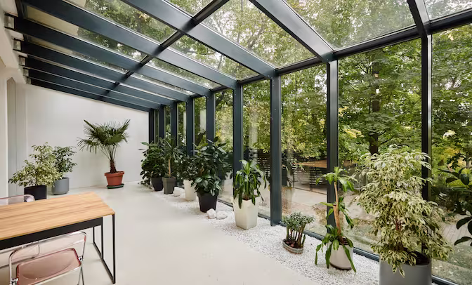 Glass-enclosed conservatory installation featuring a stylish sofa and chairs, perfect for relaxation and enjoying nature.