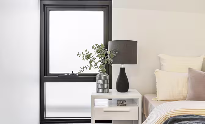 Corner room with light wooden flooring and open white-framed windows, offering natural light and views of green trees outside.