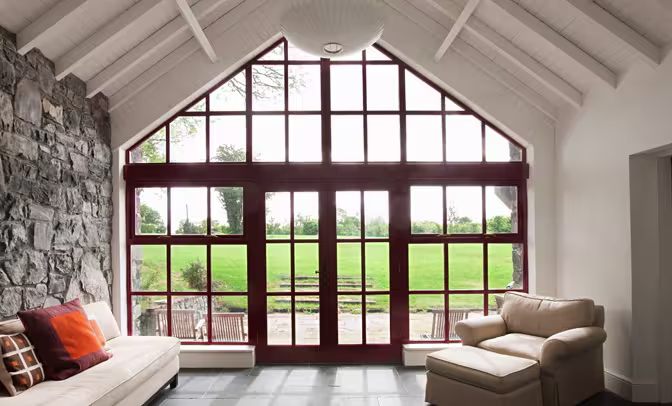 Elegant black-framed glass doors opening to a manicured garden with lush hedges and trees, blending indoor charm with outdoor greenery.