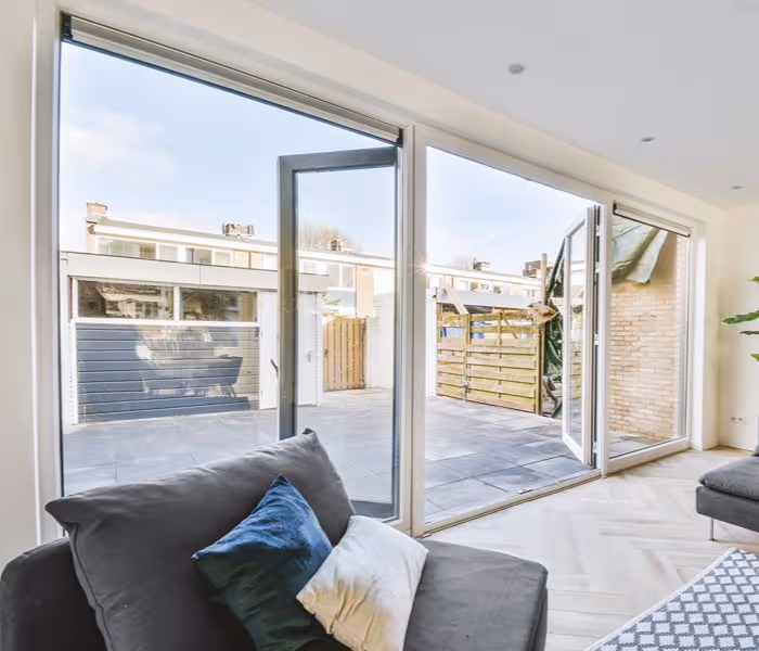 Living room with dark sofa facing large glass doors opening to a tiled outdoor patio.