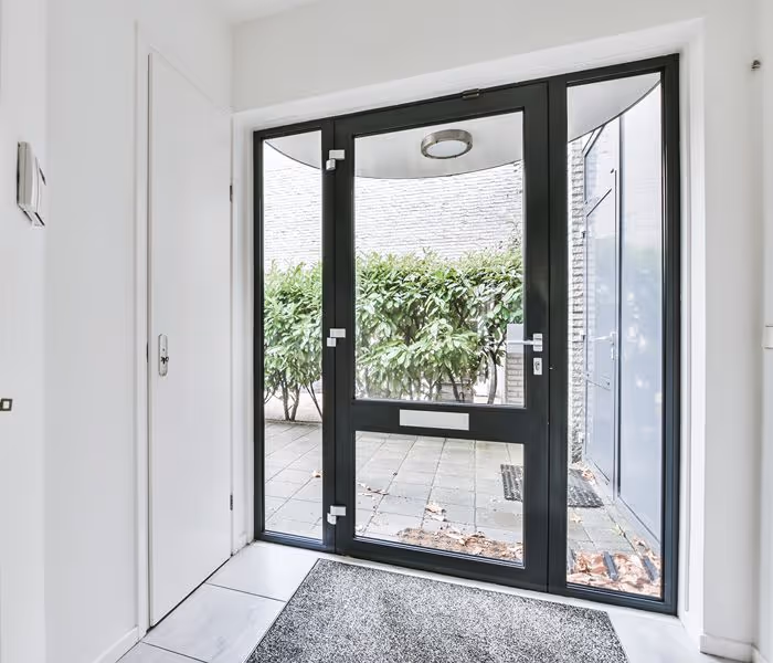 Blue front door with decorative panels and top window, set against white panelled wall with nearby hooks and a partially visible bench.