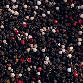 Close-up of mixed peppercorns including black, white, and red on a dark surface.