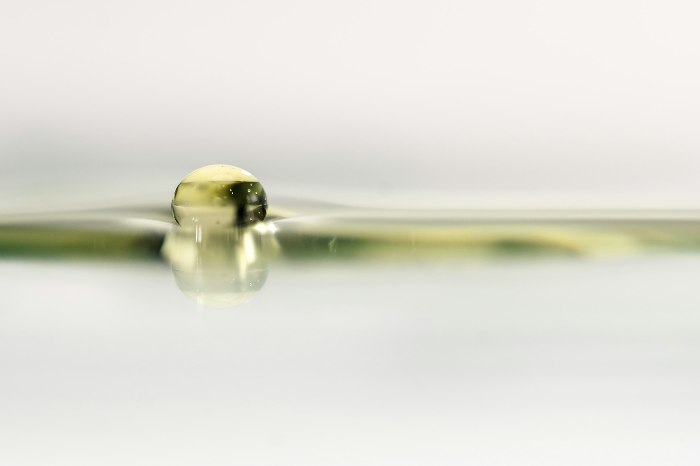 Close-up of a single cosmetic oil droplet spreading over a smooth surface, illustrating purity, fluidity, and emollient behavior.