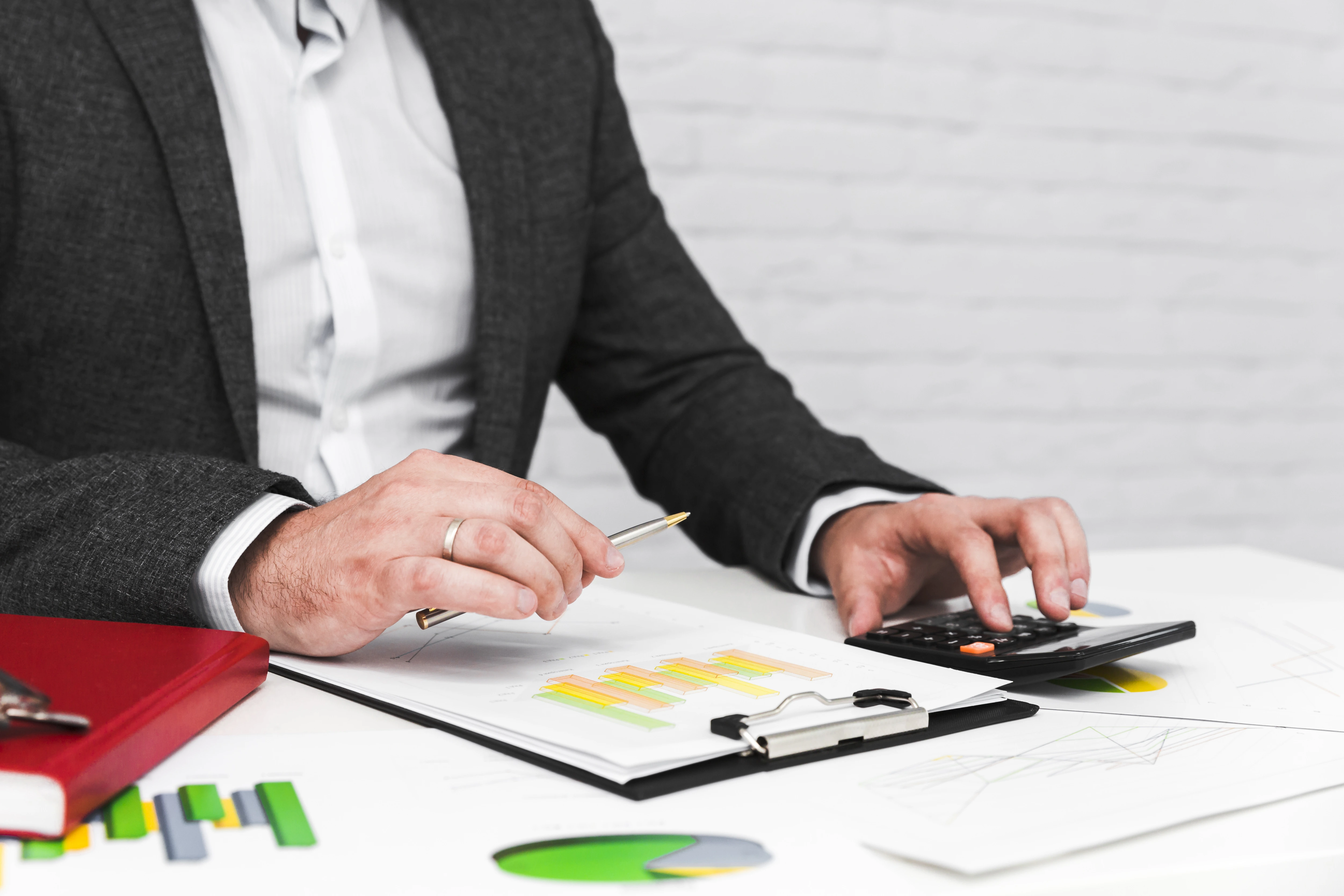 A businessman in a suit working at his desk, analyzing financial documents and using a calculator.