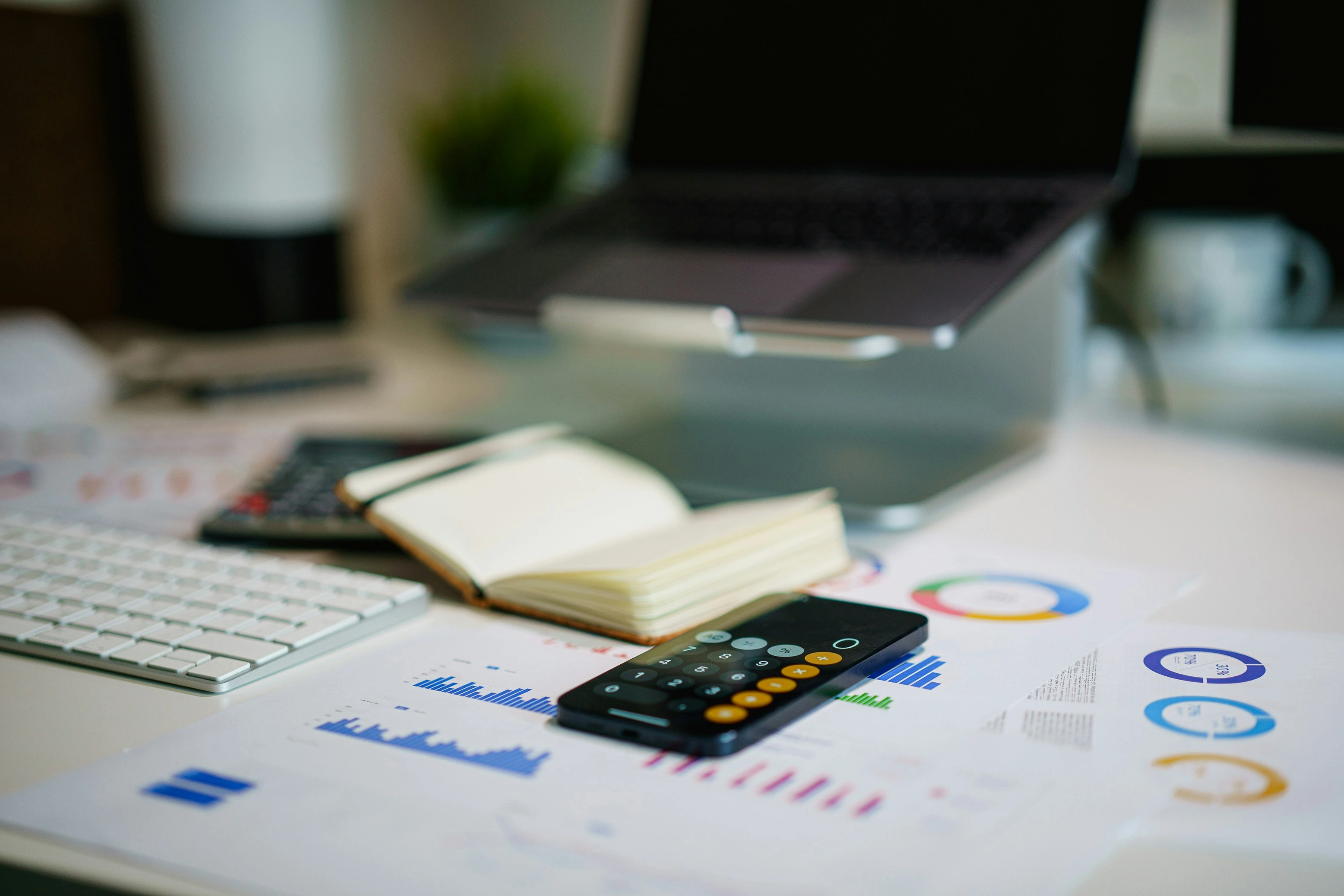 A close-up of a modern office desk with financial reports, a calculator, an open notebook, and a laptop.