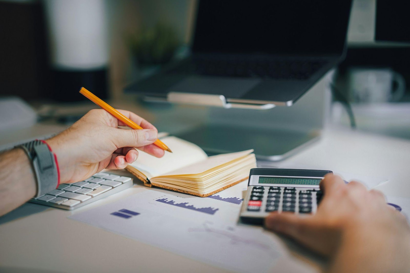 A person taking notes while using a calculator, analyzing financial documents.