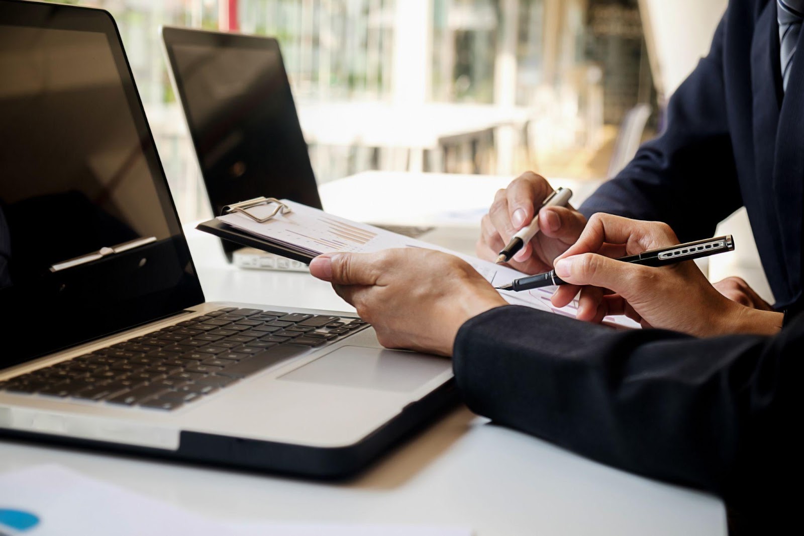 Two professionals in business attire seated at a table, collaborating over a laptop.