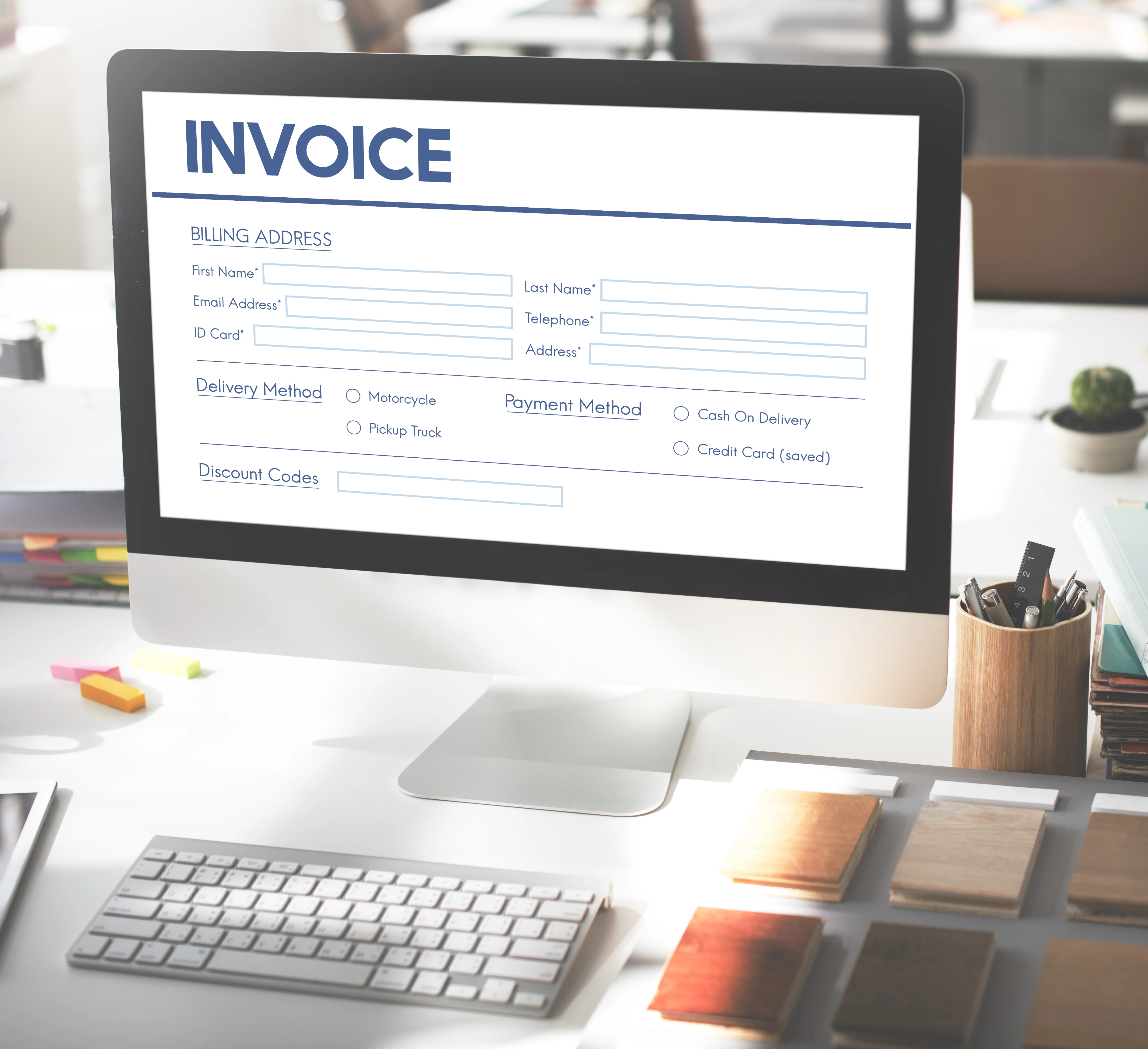 Invoice software on a desktop monitor set on a white table, surrounded by stationery.