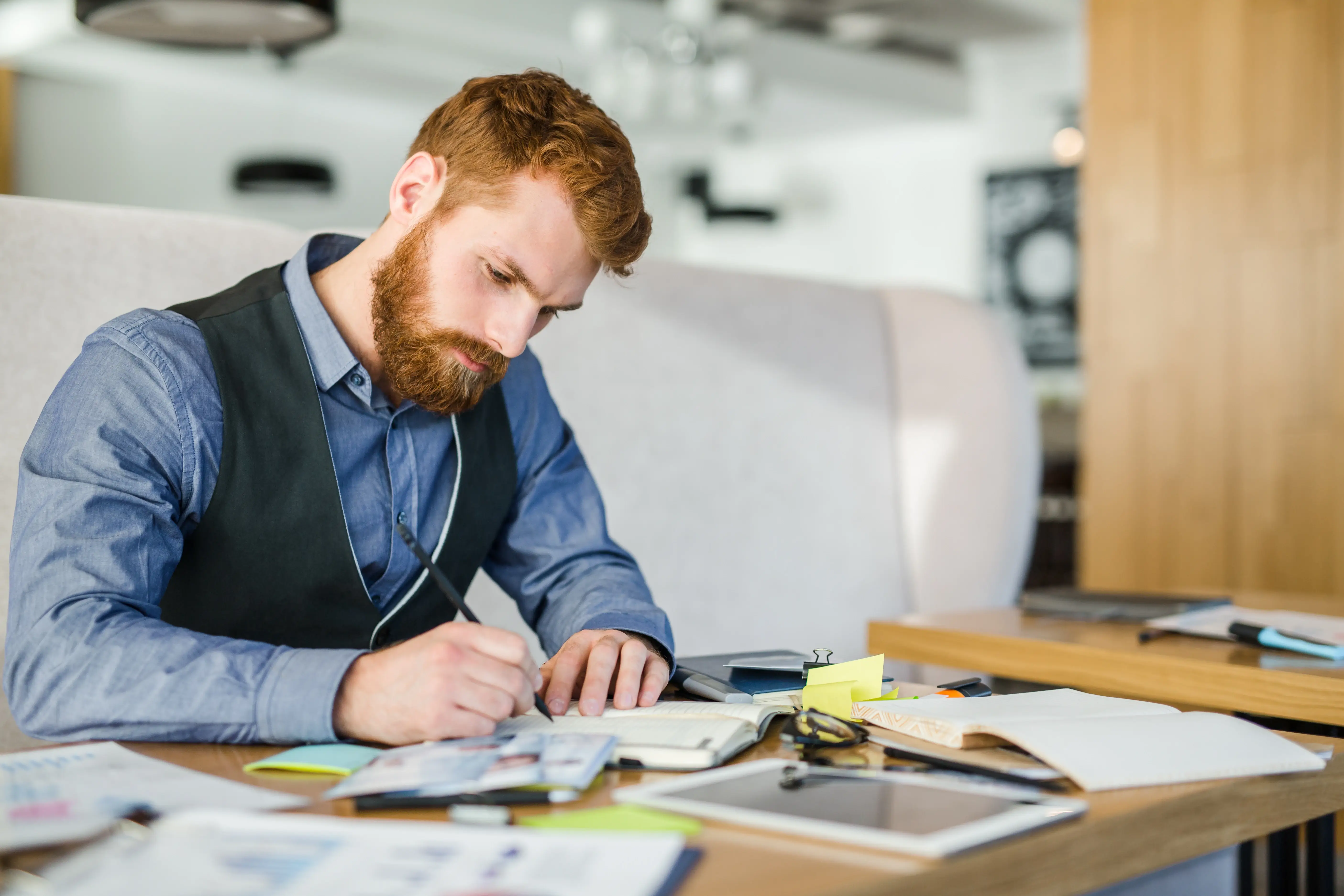 Person working through paperwork at their desk, sitting in front of their laptop and writing on a stack of papers.