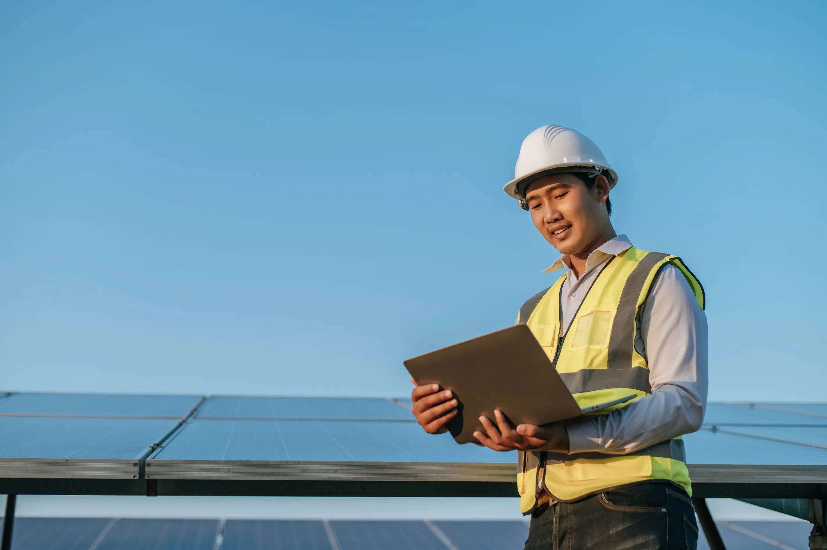 Field service professional using a a laptop while standing next to a grid of solar panels.