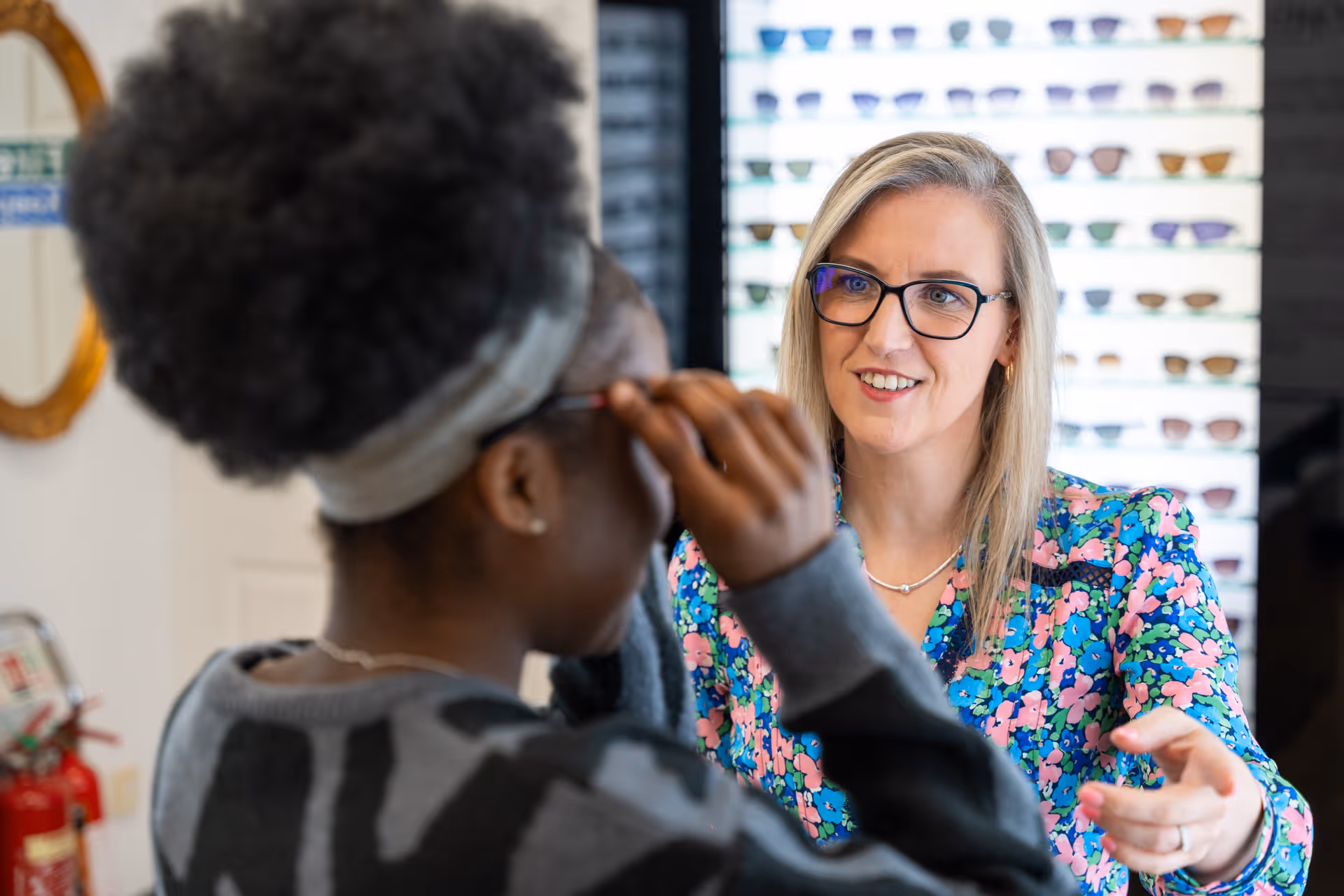 Optometrist helping customer try on glasses in eyewear store