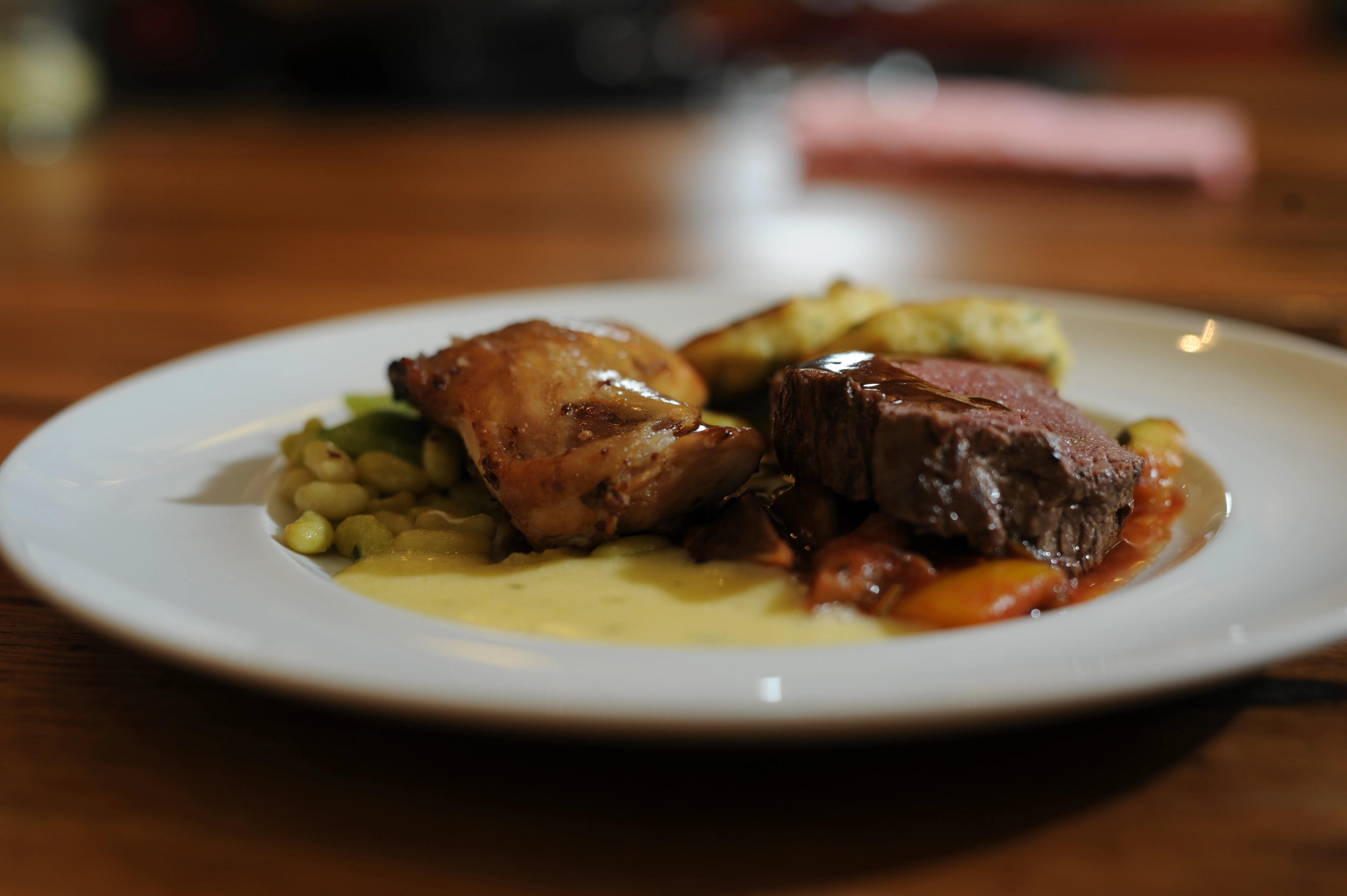 Ein Teller mit Fleisch, Soße, gebackenen Kartoffeln und Gemüse auf einem Holztisch.