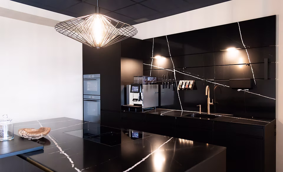 Moderne schwarze Muhlack Küche mit Marmorarbeitsplatten, Induktionskochfeld, Spüle und goldfarbener Armatur.