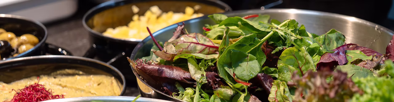 Frische Blattsalate und verschiedene Beilagen in Schalen auf einem gedeckten Tisch.