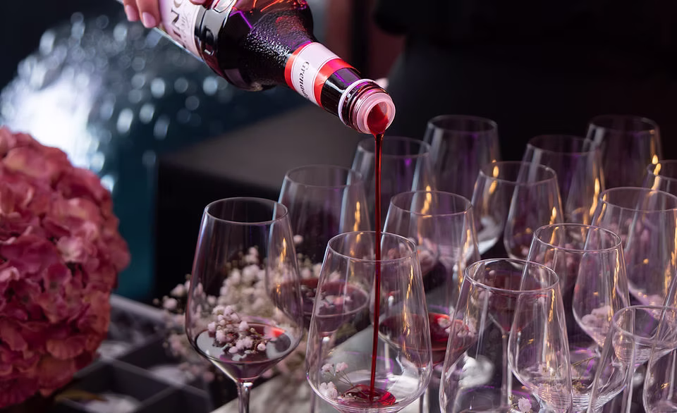 Rotwein wird in mehrere Weingläser mit Blütendekor bei einer Verkostung gegossen.