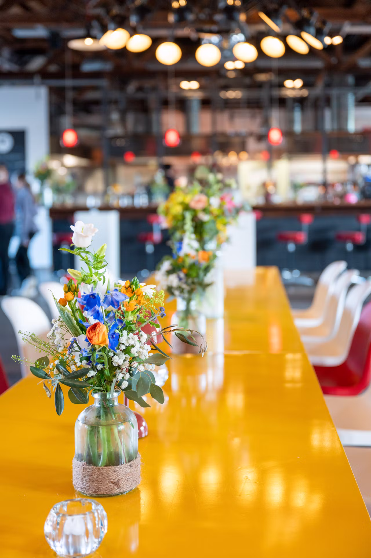 Bunte Blumen in Glasvasen auf gelbem Tisch in modernem Restaurant mit Stühlen und Deckenleuchten.