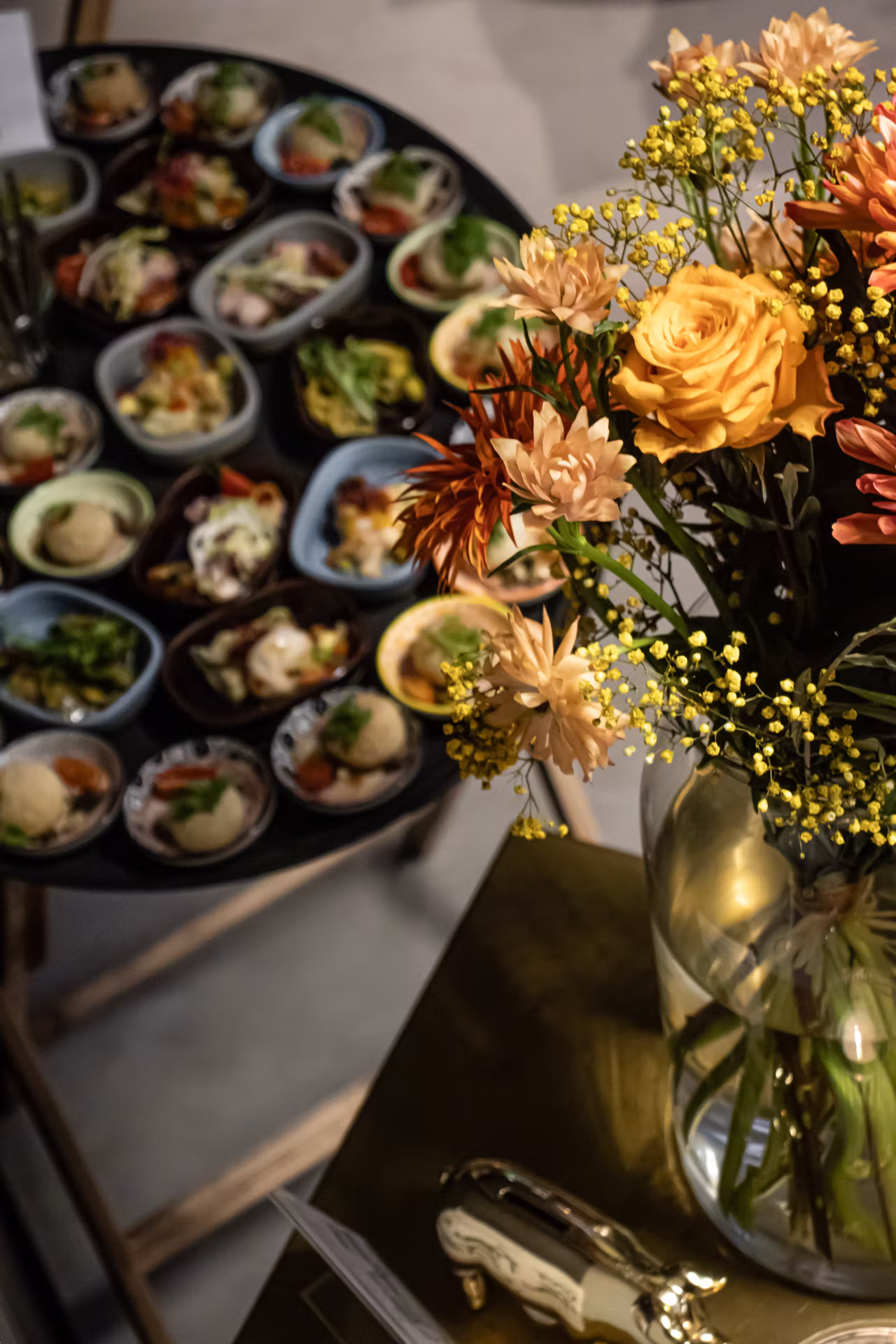 Vase mit gelben und orangefarbenen Blumen neben einem Tablett mit kleinen Schalen voller Vorspeisen.
