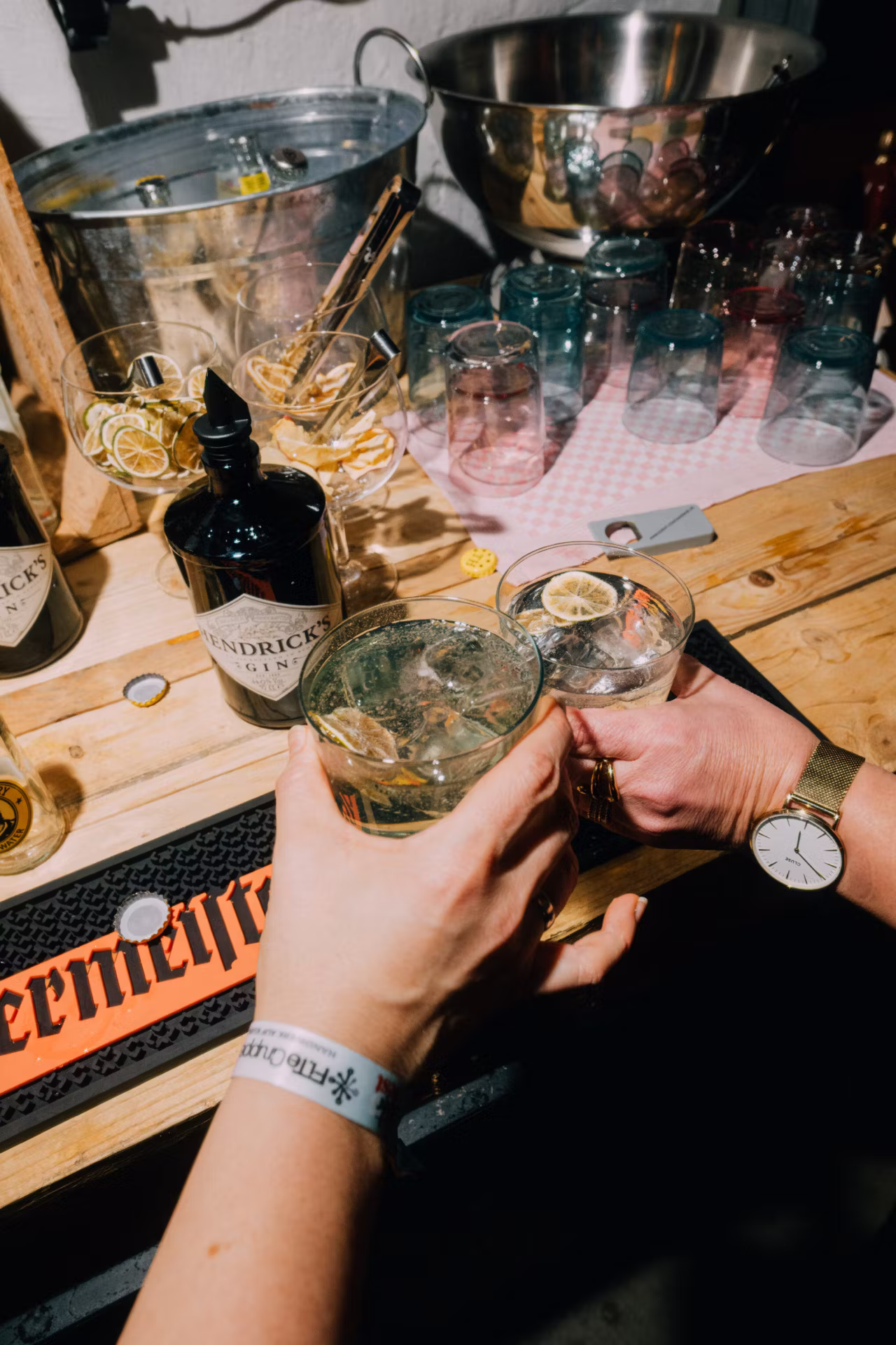 Zwei Hände stoßen mit Gin-Tonic-Gläsern über einer Theke mit Hendrick's Gin-Flasche an.