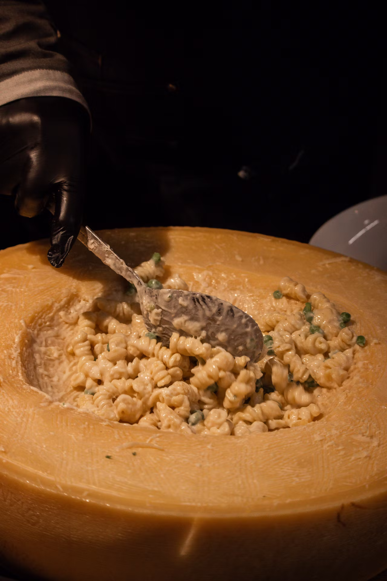 Person rührt cremige Pasta mit Erbsen in einem ausgehöhlten großen Käselaib.