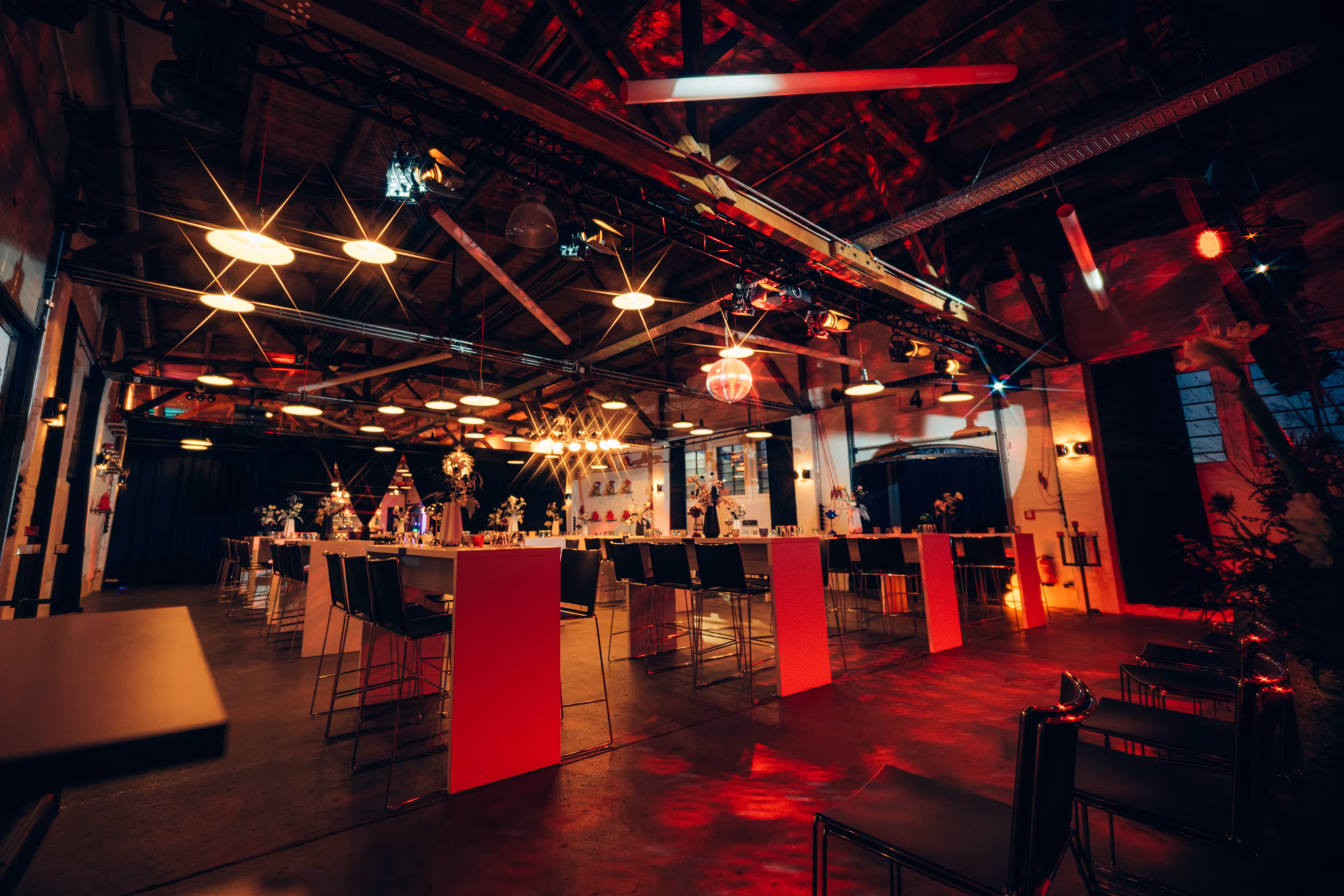 Moderne Eventlocation mit hohen Tischen, Barhockern, warmem Licht und Weihnachtsdeko.